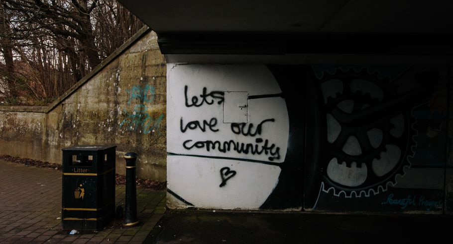 Underneath an overpass with graffiti on the wall saying "Lets love our community"