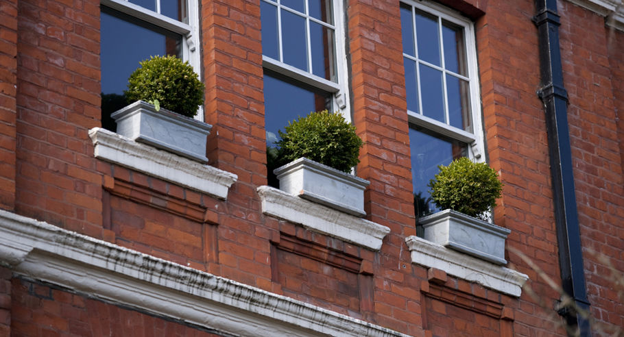 Plants sitting on the exterior windows of a red brick apartment building